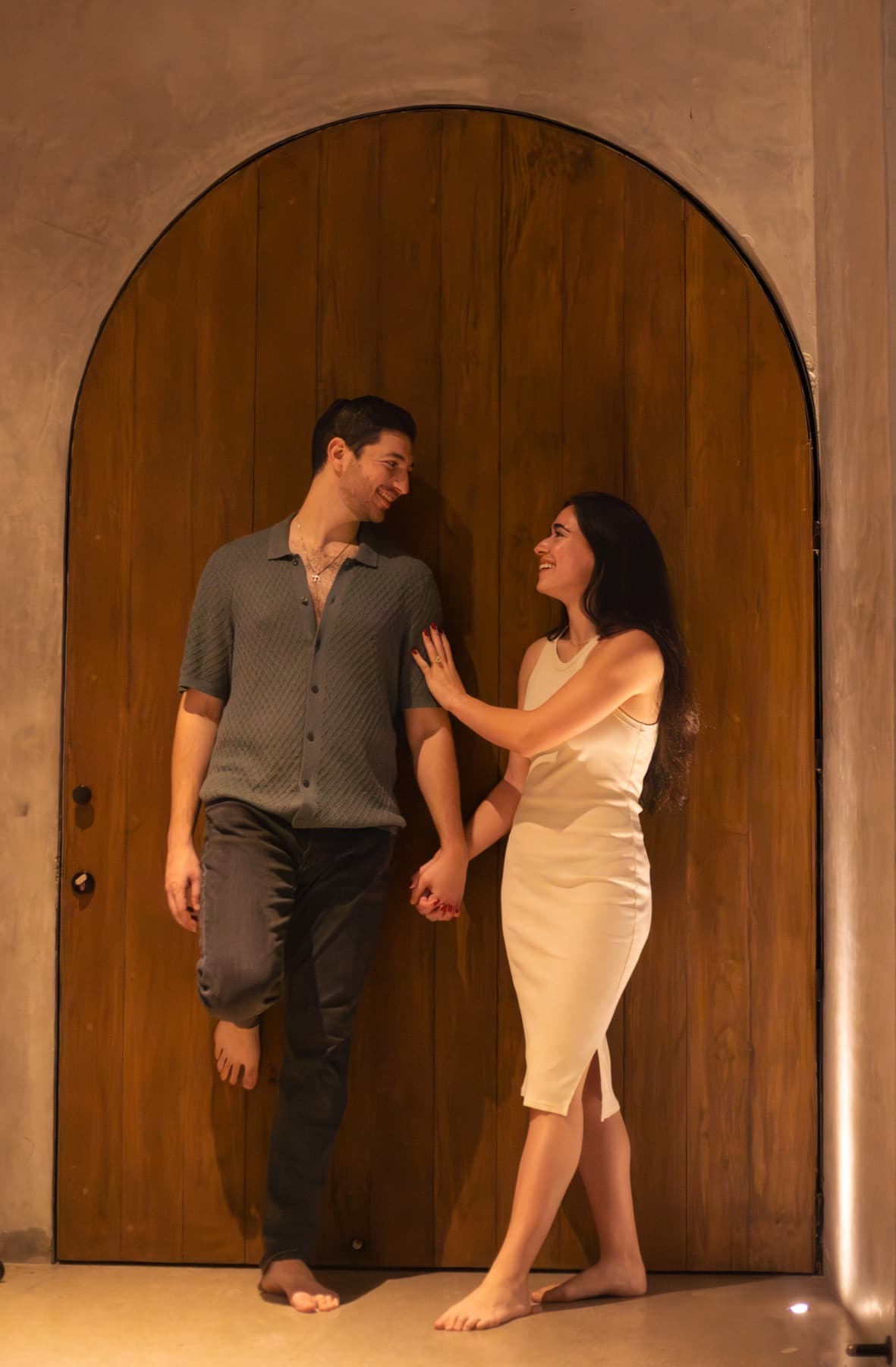 Carmela and Eden smiling together in front of an arched wooden door